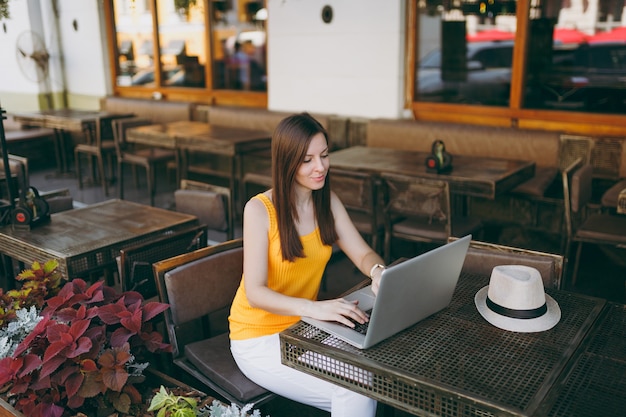 Woman in outdoors street coffee shop cafe sitting at table working on modern laptop pc computer, relaxing in restaurant during free time