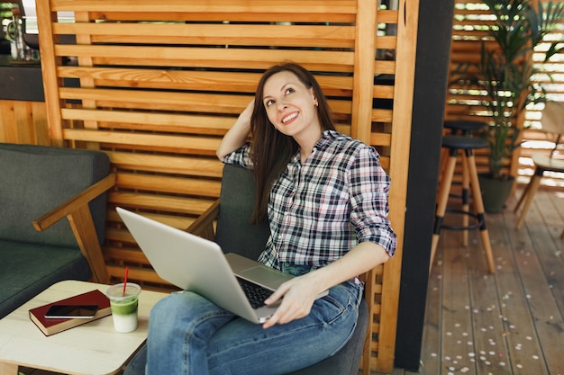 Woman in outdoors street summer coffee shop wooden cafe sitting in casual clothes, working on modern laptop pc computer