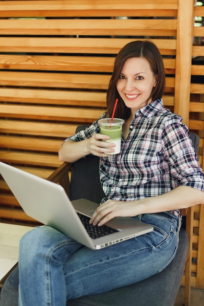 Woman in outdoors street summer coffee shop wooden cafe sitting in casual clothes, working on modern laptop pc computer