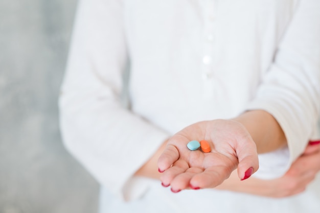 Woman outstretching hand with two colorful pills holding hand on belly. pain medication and health problems