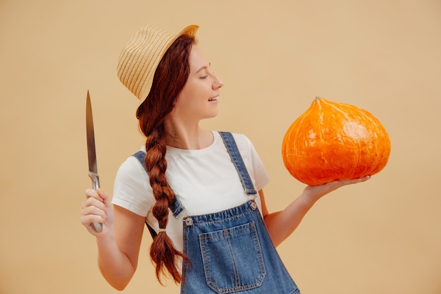 Woman in overalls with a sharp knife on yellow background is going to cut lantern out of a pumpkin