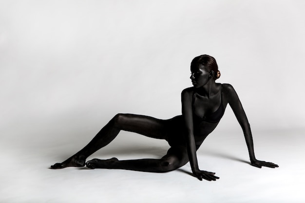 woman painted black paint lying on a white background in the Studio