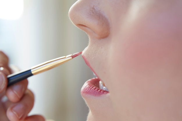 Woman painting her lips pink with a brush