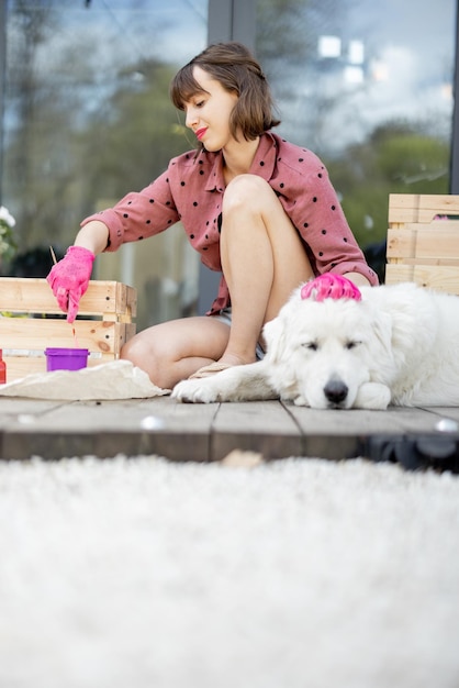 Woman painting wooden box sitting with dog on terrace