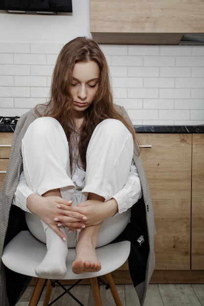 Woman in pajamas and home interior sitting in the kitchen with one sock