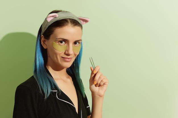 Woman in pajamas with eye patches on pastel green background