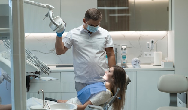 Woman patient at the dentist for a checkup. The doctor directs the lamp to the woman's face