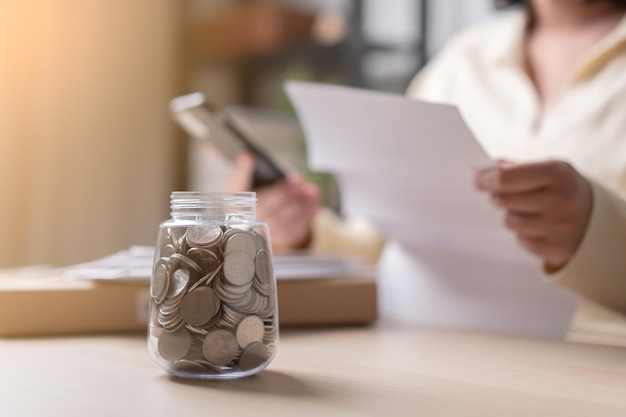 Woman pay the bills using mobile phone focus at coins in a jar as concept of saving for expenses