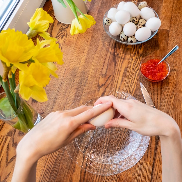 Woman peeling boiled egg on wooden background