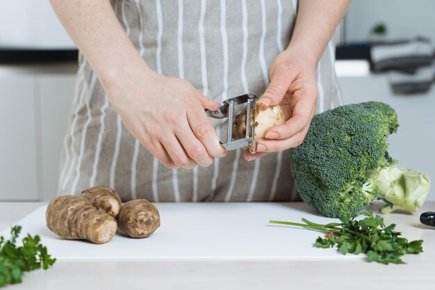 Woman peeling Jerusalem artichoke or sunroot in the kitchen