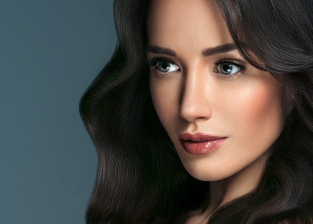 Woman perfect hair beautiful female portrait over blue background. Brunette haircare long curly hairstyle beauty concept. Studio shot.