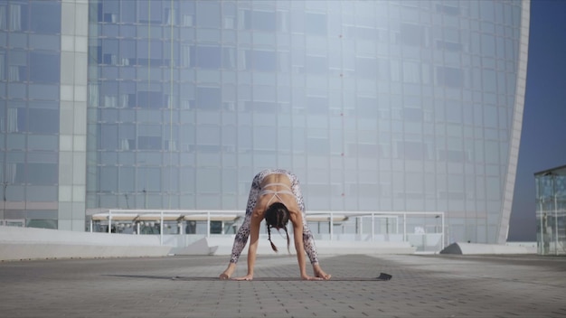 Woman performing yoga in urban street Lady doing garland pose on mat outdoors