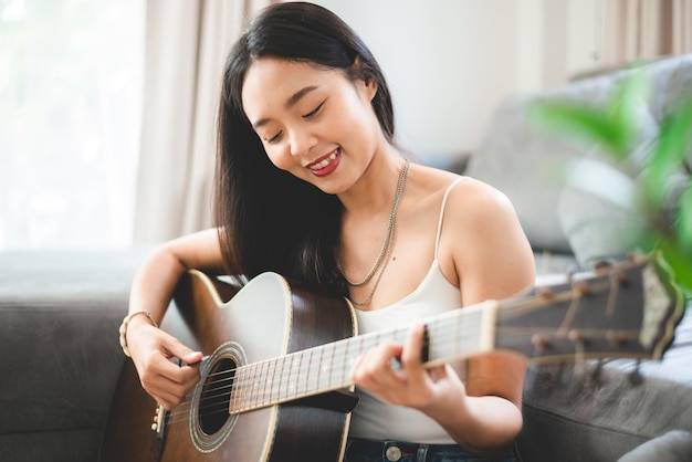 Woman person playing acoustic guitar music instrument at home, young Asian musician girl lifestyle