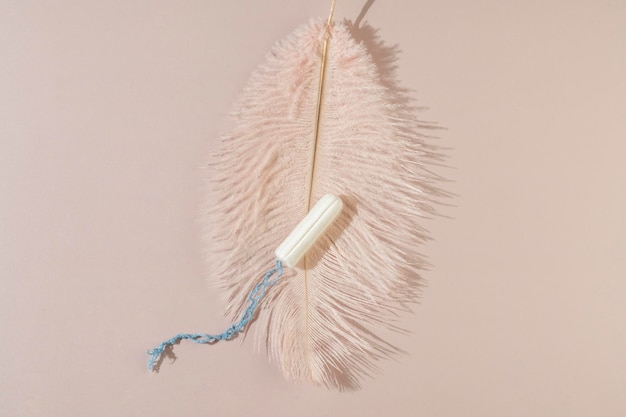 A woman personal hygiene cotton tampon lying on a light pink feather as a concept of freshness