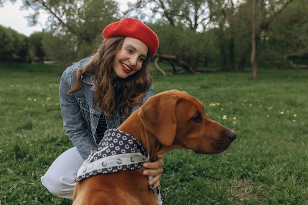 woman petting brown Rhodesian Ridgeback dog in bandana while sitting on green lawn