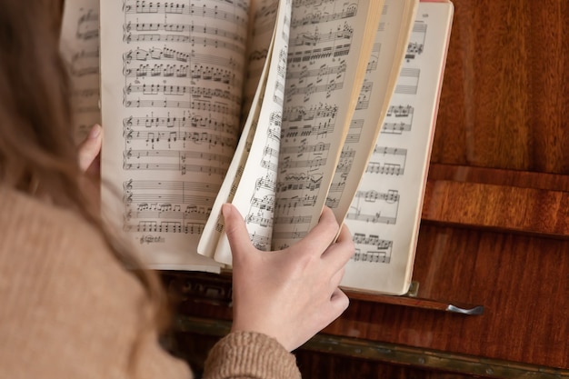 A woman pianist sits at the piano leafing through the notes.