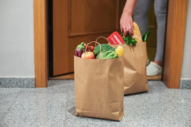 A woman picks up a bag of food at the door of her house. Coronavirus. Quarantine. Stay at home, Online shopping. Vegetables and fruits delivery during quarantine and self-isolation