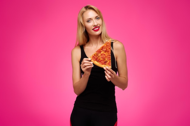 Woman on a pink background holds a pizza in her hands and smiles Concept of healthy and junk food