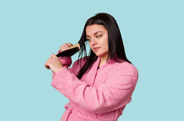 Woman in pink bathrobe getting ready grooming her hair with a comb looking pretty