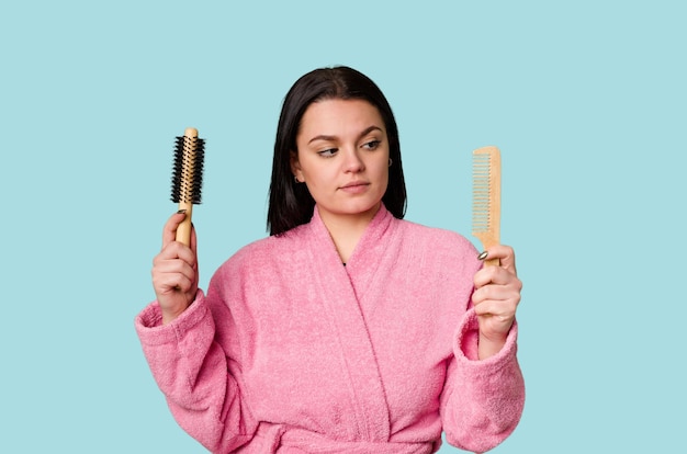 A woman in a pink bathrobe holding a hairbrush and comb with a towel wrapped around her head