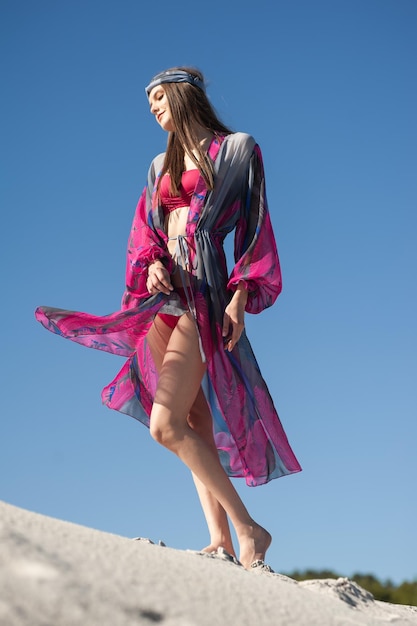 A woman in a pink bikini stands on a sand dune.