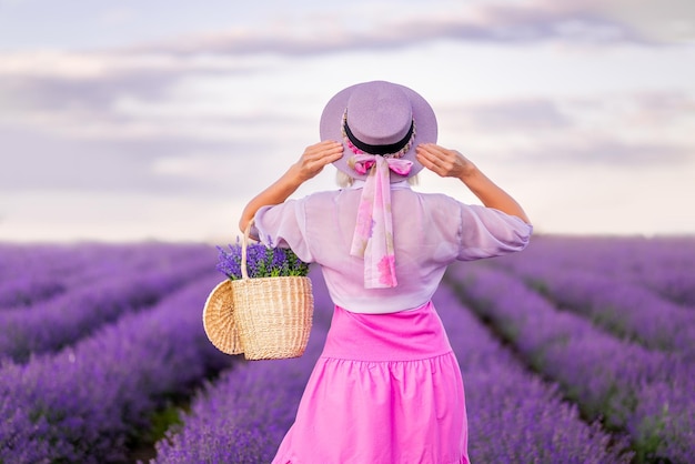 Woman in a pink dress and a lilac hat looks at the beautiful sky in a field with lavender Sunset in Provence View from the back