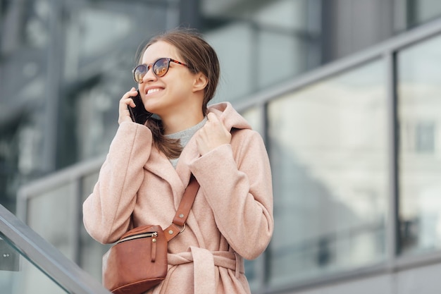 Woman in pink dress talking to smarthone outdoor on grey urban city background