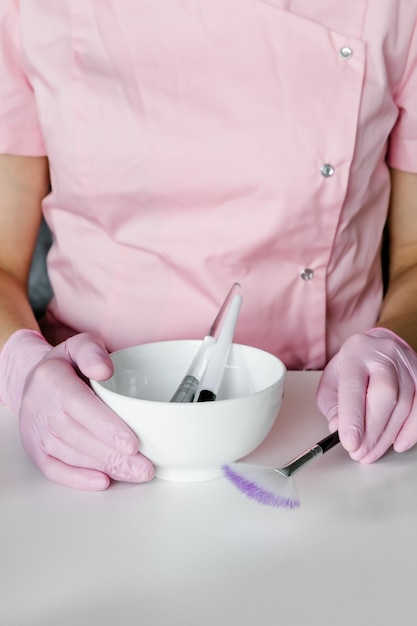 Woman in pink gloves with white bowl and cosmetic brushes