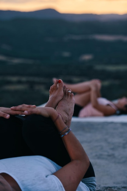 A woman in a pink top and leggings stretches on a beach with a mountain in the background.