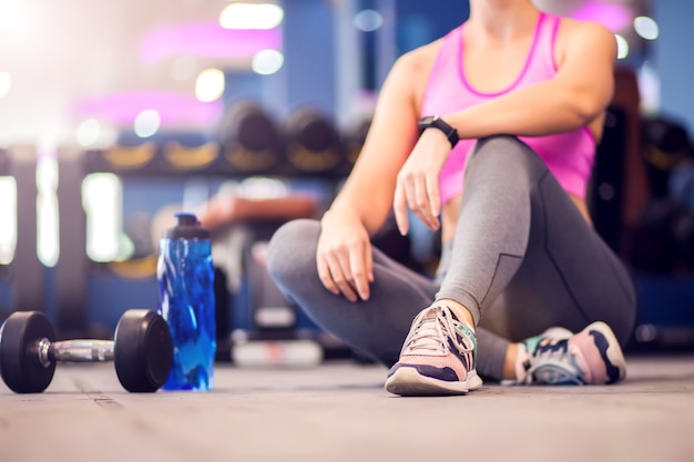 Woman in a pink top and short blond hair resting in the gym. People, fitness and health care concept