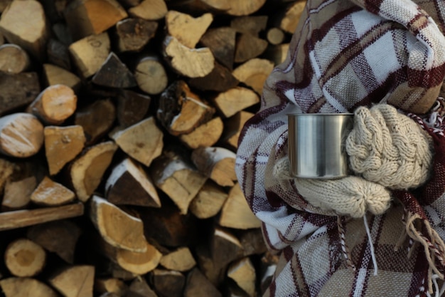 Woman in plaid holds metal cup against the background of firewood