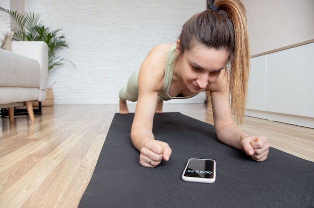 woman in plank pose looking at timer on her smartphone