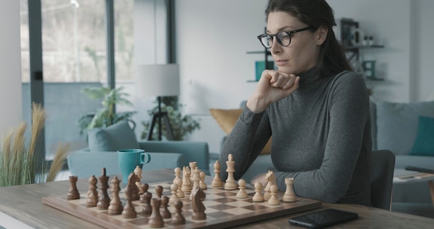 Woman playing chess at home she is thinking and looking at the chessboard