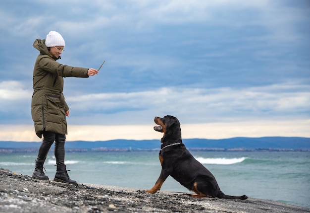 Woman playing with rottweiler dog in cold weather on the beach