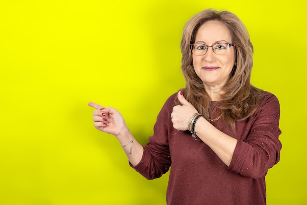 Woman pointing empty space and thumb up with smiling face yellow studio background