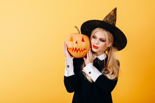 Woman portrait against a yellow   holding pumpkin and looking on it smiling