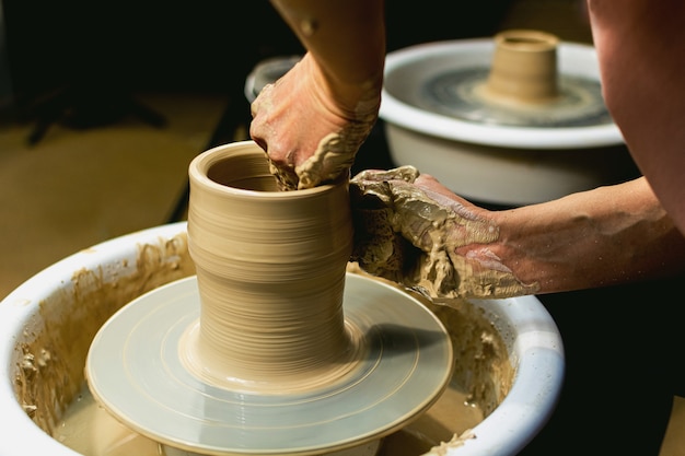 The woman potter's hands formed by a clay pot on a potter's wheel. The potter works in a workshop. High quality photo