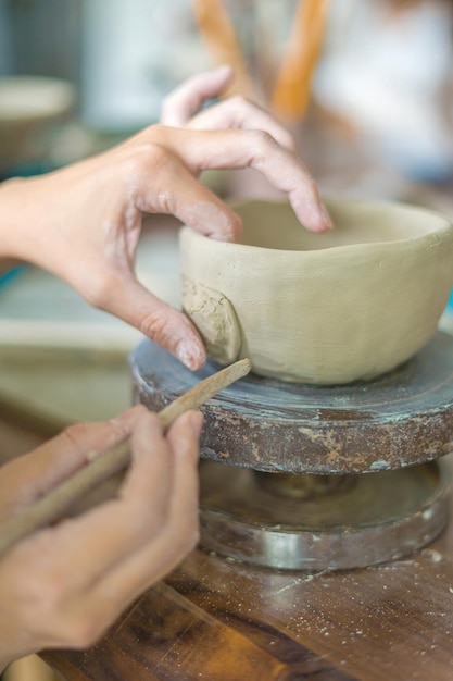 Woman potter working on potters wheel making ceramic pot from clay in pottery workshop art concept Focus hand young woman attaching clay product part to future ceramic product Pottery workshop