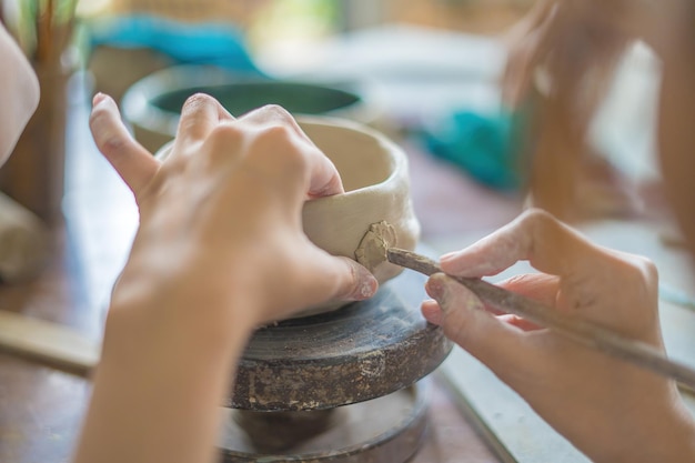 Woman potter working on potters wheel making ceramic pot from clay in pottery workshop art concept Focus hand young woman attaching clay product part to future ceramic product Pottery workshop