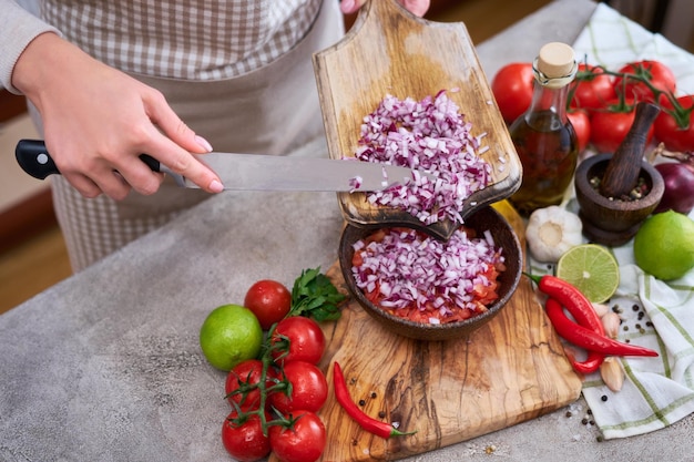 Woman pouring chopped onion to wooden bowl with tomatoes