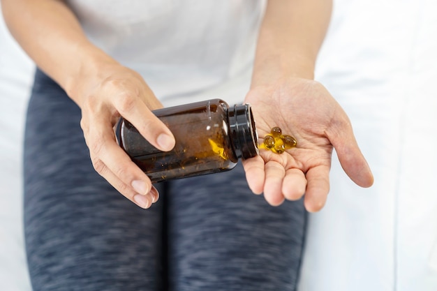 Woman pouring fish oil capsule or cod liver oil of high omega 3 vitamin pill on hand. Healthy lifestyle.