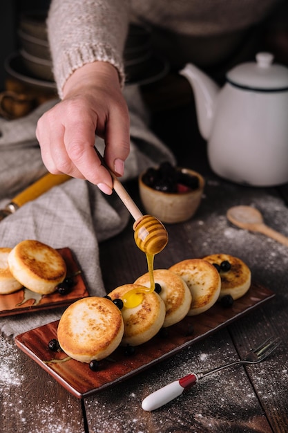 Woman pouring honey onto delicious cottage cheese pancakes