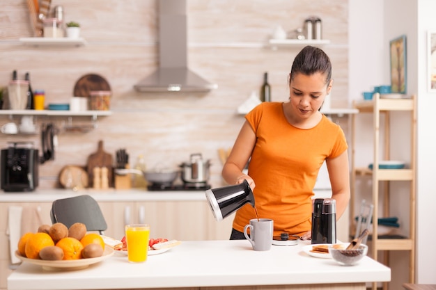 Woman pouring hot coffee in cup in the morning from pot