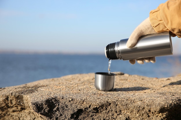 Woman pouring hot drink from thermos bottle into cup outdoors closeup