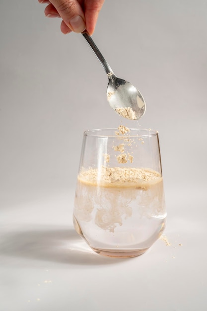 Woman pours collagen powder or protein in a glass of water on a beige background A healthy and anti aging supplement Copy space