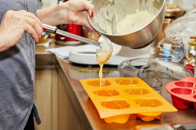 Woman pours the dough into muffin molds for making sun-dried tomato muffins.