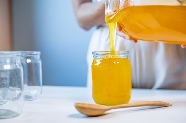 Woman pours honey into transparent jars on a white table