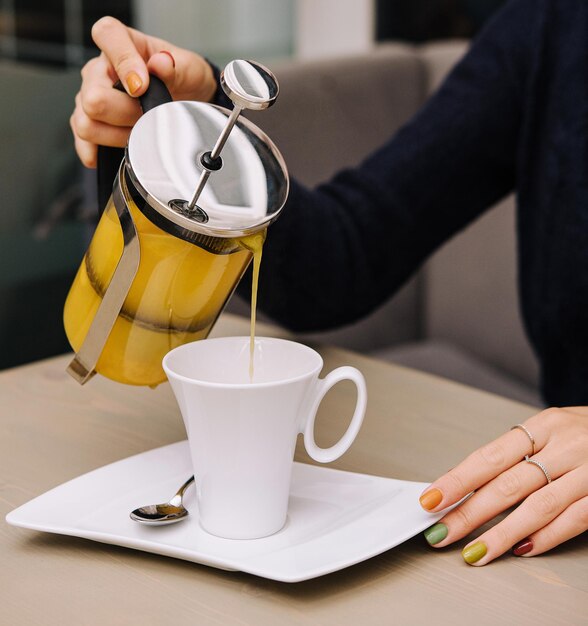 A woman pours sea buckthorn tea from a teapot into a mug