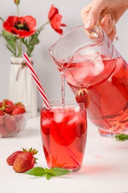 Photo a woman pours a soft drink with strawberries and ice.