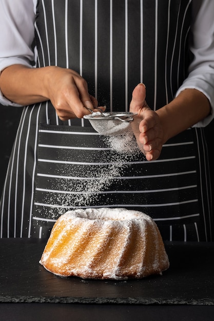 Woman powder of sugar to vanilla bundt cake on dark background